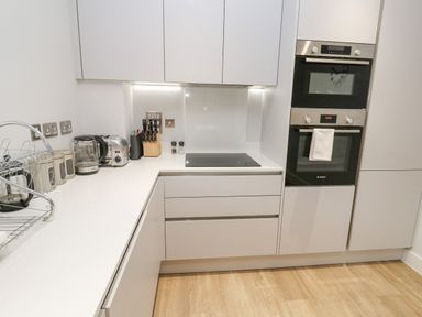 A modern kitchen with white cabinets black ovens a stove kettle toaster and knife set at Sebastians View in Falmouth