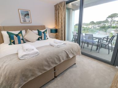 A bedroom with a bed pillows towels bedside lamp and balcony with table and chairs at Sebastians View in Falmouth