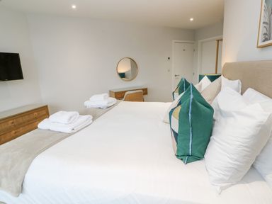 A bedroom with a bed with white sheets and green pillows a wooden dresser a wall mirror and a wall-mounted tv at Sebastian's View in Falmouth