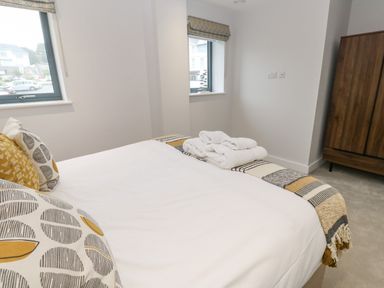 A bedroom with a bed, folded towels on the bed, two windows, and a wooden wardrobe at Sebastians View in Falmouth
