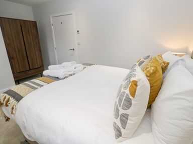 A bedroom with a bed featuring white and yellow patterned pillows a wooden wardrobe and white towels on the bed at Sebastian's View in Falmouth
