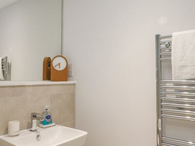 A bathroom sink with a faucet a soap dispenser a candle a clock on the countertop and a towel on a heated rack at Sebastians View in Falmouth