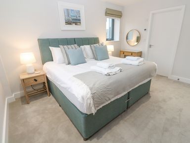 A bedroom with a double bed bedside tables lamps a round mirror and folded towels at Sebastians View in Falmouth