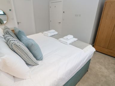 A bedroom with a bed with pillows and folded towels near white doors and a wooden wardrobe at Sebastian's View in Falmouth