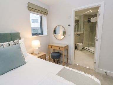 A bedroom with a bed side table lamp dressing table round mirror stool and an open door to a bathroom at Sebastians View in Falmouth