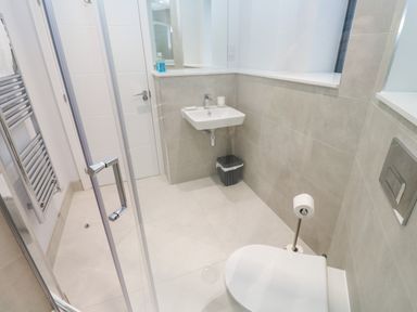 A bathroom with a shower enclosure, wall-mounted sink, toilet, towel rack, and trash bin at Sebastians View in Falmouth