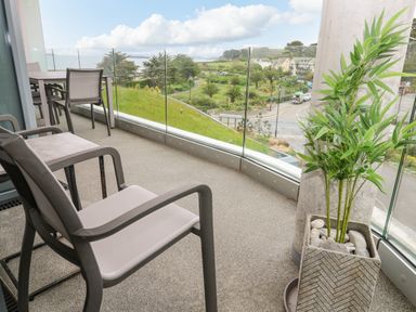 A balcony with chairs a table and a potted plant overlooking a park and houses at Sebastians View in Falmouth