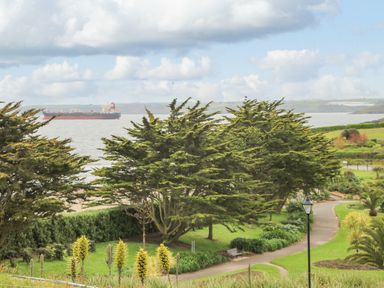 A coastal park with trees benches a pathway and a large ship on the water at Sebastian's View in Falmouth