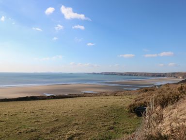 A coastal landscape with a sandy beach a grassy field and a blue sky at Coach House in Haverfordwest near Broad Haven