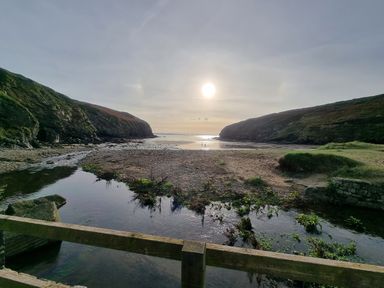 A beach with rocky cliffs on both sides and a small stream flowing under a wooden bridge at Coach House in Haverfordwest near Broad Haven