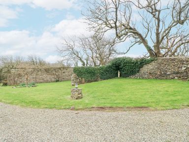 A garden with a stone wall, green grass, bare trees, and a small statue at Coach House in Haverfordwest near Broad Haven