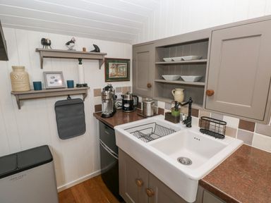 A kitchen corner with a white sink a black faucet coffee machines shelves with bowls and decorative items at Coach House in Haverfordwest near Broad Haven