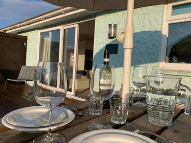 An outdoor dining table set with plates glasses a bottle of wine and a water jug on a wooden deck outside a building at Little Beach in Seaview