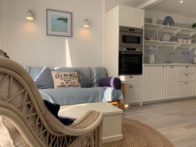 A kitchen and living area with white cabinets a blue covered sofa and a wicker chair at Little Beach in Seaview