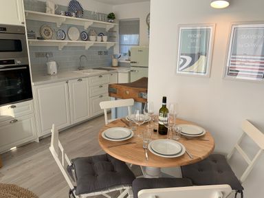 A kitchen with white cabinets wooden round dining table set for four and framed pictures on wall at Little Beach in Seaview