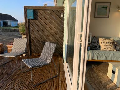 A deck with two chairs next to sliding glass doors showing a sofa with cushions and a rug inside at Little Beach in Seaview
