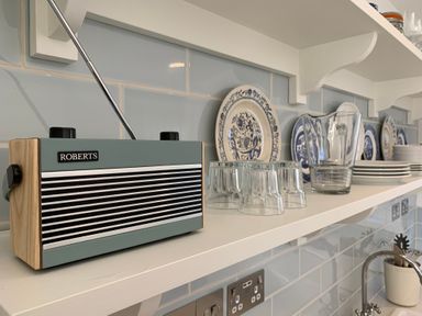 A kitchen shelf with a Roberts radio glassware and decorative plates at Little Beach in Seaview