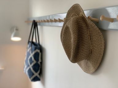 A beige woven hat and a blue tote bag hanging on a wooden peg rail mounted on a white wall in a room at Little Beach in Seaview