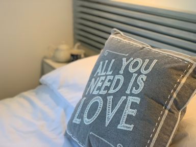A grey pillow with the words all you need is love on a bed with white sheets at Little Beach in Seaview
