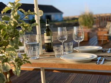 An outdoor wooden table set with two white plates two wine glasses two water glasses a water pitcher and a bottle of wine in a garden at Little Beach in Seaview