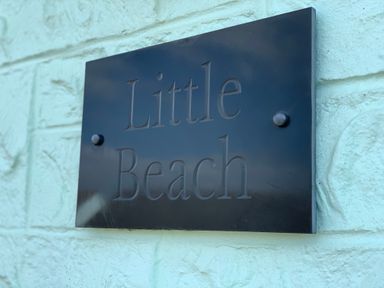 A close-up of a black sign with the text Little Beach mounted on a light blue textured wall at Little Beach in Seaview