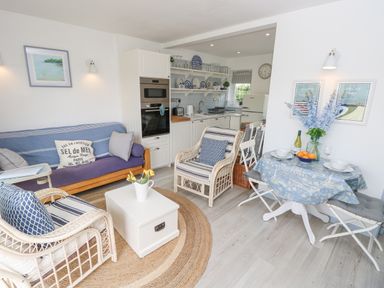 A living room with wicker chairs blue cushions a white coffee table and a small dining table with flowers at Little Beach in Seaview