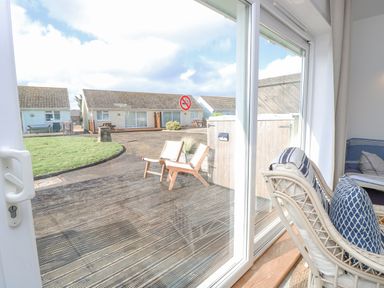 A sliding glass door opening to a wooden deck with two chairs and bushes with small houses and a grassy area outside at Little Beach in Seaview