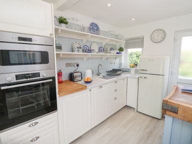A kitchen area with white cabinets and appliances including an oven, refrigerator, toaster, and kettle with shelves holding dishes and glassware at Little Beach in Seaview
