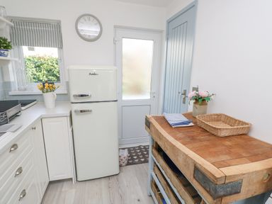 A kitchen with a white fridge a wooden countertop with a basket and flowers and a door at Little Beach in Seaview