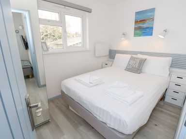 A bedroom with a double bed and white linens two bedside tables with lamps and a window at Little Beach in Seaview