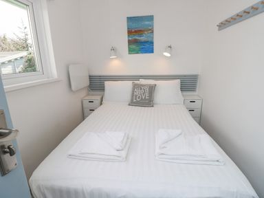 A bedroom with a bed with white bedding and towels on top a window to the left and a painting on the wall at Little Beach in Seaview
