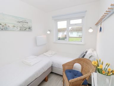 A bedroom with two single beds a wicker chair with a blue cushion and a window overlooking other houses at Little Beach in Seaview