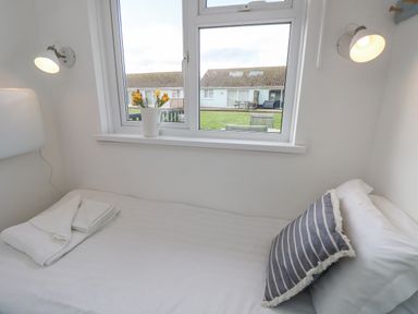A single bed with white sheets and a striped pillow under a window with flowers in a pitcher lamp on each side at Little Beach in Seaview