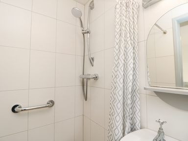 A bathroom shower area with a handheld showerhead curtain rail and a mirror above a sink at Little Beach in Seaview