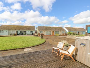 Three detached single-story houses with patios and picnic tables a grassy area and wooden chairs on a deck in front of the houses at Little Beach in Seaview
