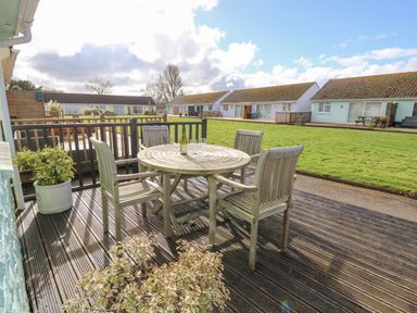 A wooden deck with a round table and four chairs with wine and glasses overlooking a grassy area and bungalow houses at Little Beach in Seaview