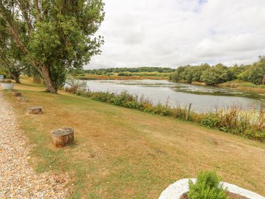 A grassy riverside area with wooden stools along a gravel path and trees near Little Beach in Seaview