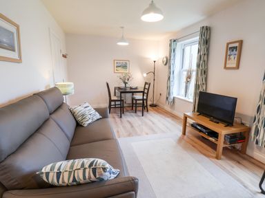 A living room with a grey sofa two chairs a small dining table a TV on a wooden stand and patterned curtains at Kittiwakes The Bay  Filey