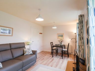 A living room with a gray sofa and pillows a small dining table with two chairs and patterned curtains at Kittiwakes in The Bay Filey