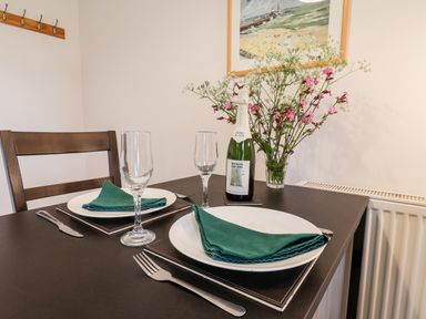 A dining table set for two with plates green napkins wine glasses cutlery a bottle of wine and a flower vase at Kittiwakes The Bay - Filey