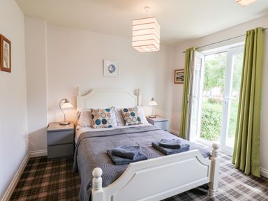 A bedroom with a white bed green curtains and bedside tables with lamps at Kittiwakes The Bay Filey