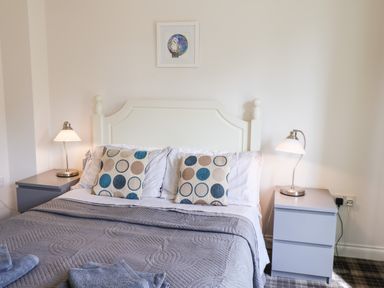 A bedroom with a white bed headboard gray bedside tables lamps and patterned cushions at Kittiwakes in The Bay Filey
