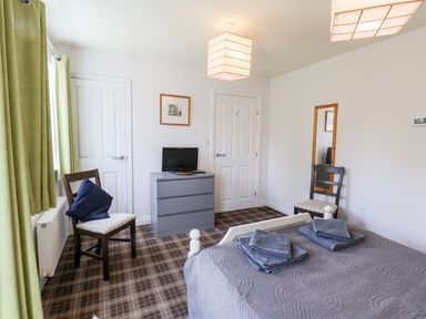 A bedroom with a bed covered with grey bedding and towels two chairs a dresser with a small tv and green curtains at Kittiwakes The Bay Filey