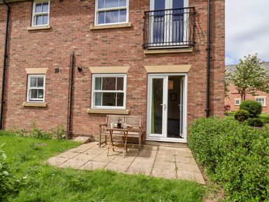 A backyard with a small patio table and two chairs in front of a brick house with windows and a glass door at Kittiwakes The Bay Filey