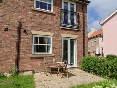 An outdoor patio area with a wooden bench and small table with food in front of a brick house with windows and a door at Kittiwakes The Bay - Filey