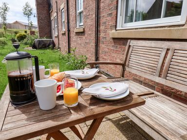 A wooden table with coffee pot cups croissants orange juice and napkins next to a wooden bench at Kittiwakes The Bay - Filey