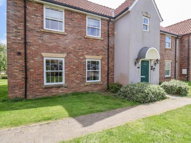 Front view of a brick and stucco house with green front door and windows surrounding a paved walkway at Kittiwakes The Bay - Filey