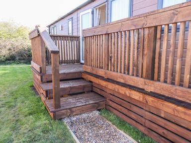 A wooden deck with stairs and railing attached to a building with grassy lawn and gravel path