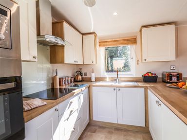 A kitchen with white cabinets wooden countertops a window over the sink and appliances including a microwave toaster and kettle at Marigold Lodge in Runswick Bay near Staithes