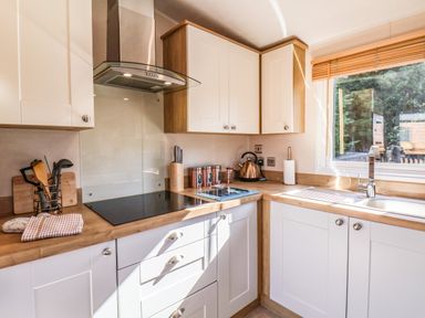A kitchen with white cabinets wooden countertops a stove kettle knives and a window at Marigold Lodge in Runswick Bay near Staithes